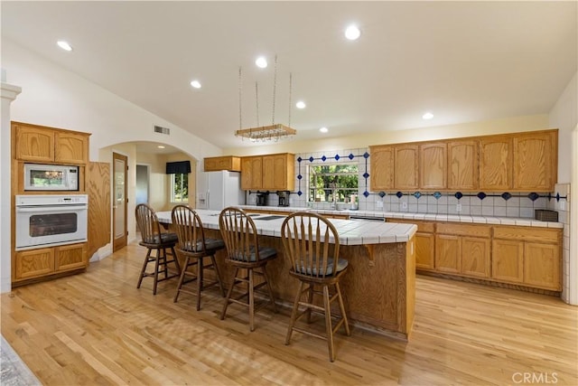 kitchen featuring tile countertops, white appliances, decorative backsplash, light hardwood / wood-style floors, and a kitchen island