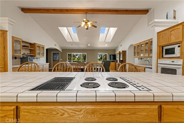 kitchen featuring a skylight, white appliances, ceiling fan, high vaulted ceiling, and beamed ceiling