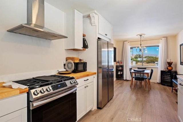 kitchen featuring wood counters, white cabinets, wall chimney range hood, appliances with stainless steel finishes, and decorative light fixtures