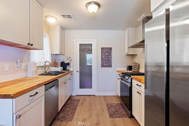 kitchen with wood counters, appliances with stainless steel finishes, white cabinets, and sink