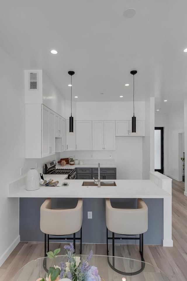 kitchen with a kitchen bar, kitchen peninsula, stainless steel range with gas stovetop, and decorative light fixtures