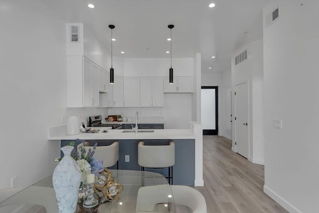 kitchen featuring decorative light fixtures, a kitchen bar, sink, stainless steel range oven, and white cabinets