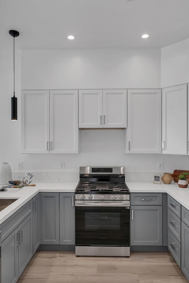 kitchen with gray cabinets, light hardwood / wood-style floors, hanging light fixtures, and stainless steel gas range oven