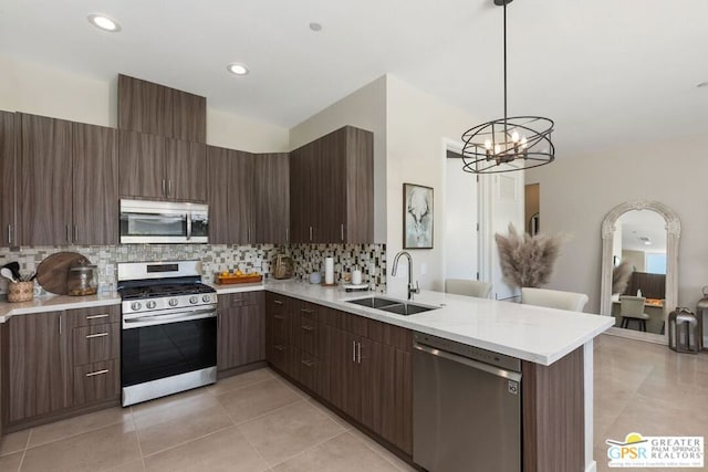 kitchen featuring sink, stainless steel appliances, kitchen peninsula, pendant lighting, and dark brown cabinets