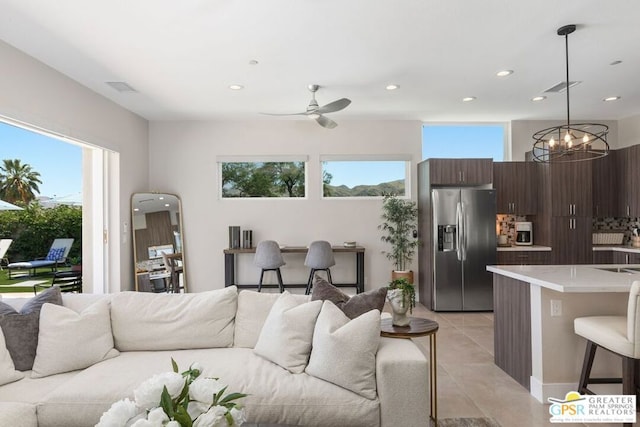 tiled living room with ceiling fan with notable chandelier and a healthy amount of sunlight