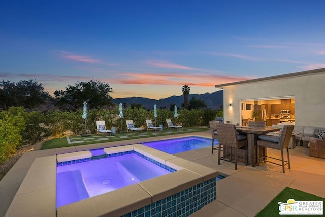 pool at dusk with a patio area, a mountain view, and an in ground hot tub