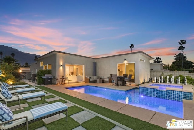 pool at dusk featuring an in ground hot tub, a mountain view, a patio, and a grill