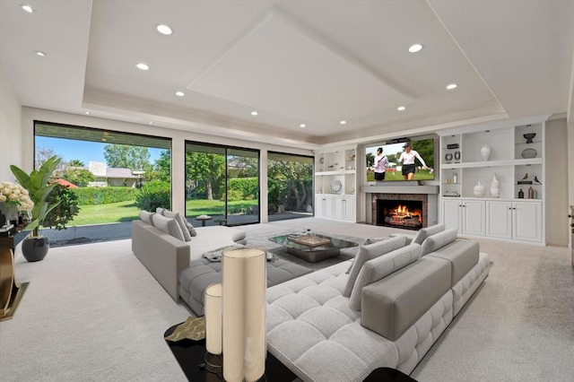 living room with a raised ceiling, light colored carpet, and built in shelves