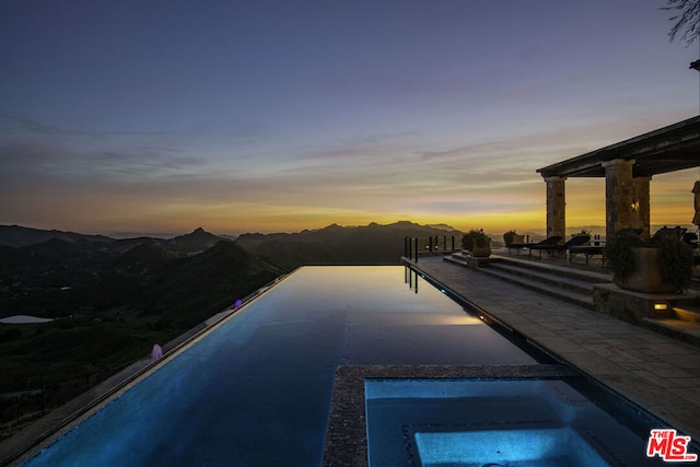 pool at dusk featuring an in ground hot tub