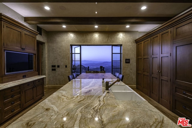 kitchen featuring light stone counters, wood-type flooring, dark brown cabinets, beamed ceiling, and sink