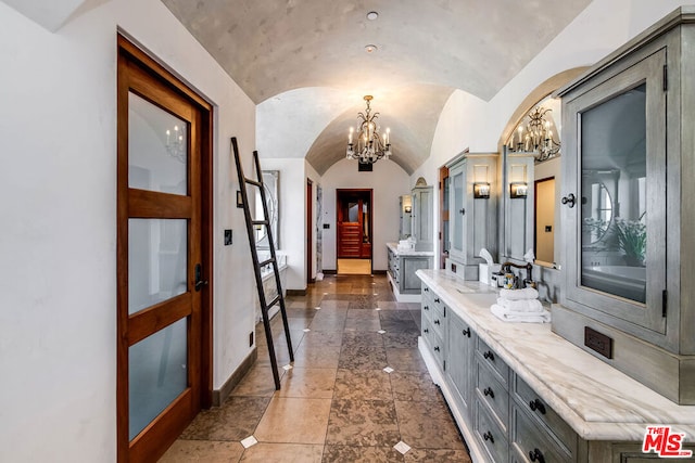 entrance foyer featuring a notable chandelier, sink, lofted ceiling, and dark tile flooring