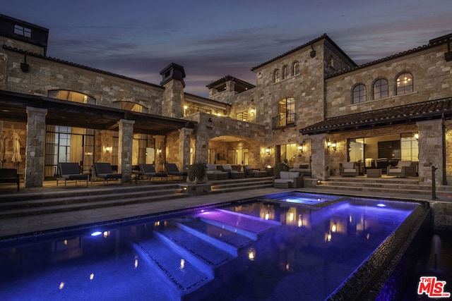 pool at dusk featuring an in ground hot tub, a patio area, and an outdoor hangout area