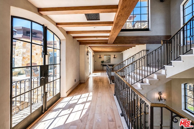 corridor featuring beam ceiling, light hardwood / wood-style floors, and french doors