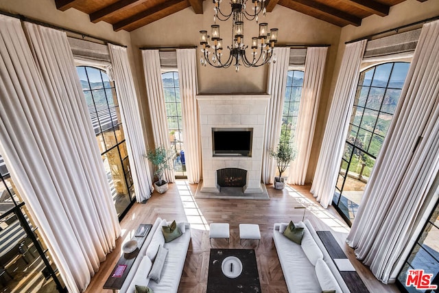 living room with beamed ceiling, high vaulted ceiling, a tiled fireplace, and an inviting chandelier