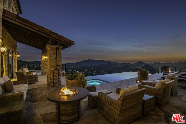 patio terrace at dusk featuring an outdoor living space with a fire pit, a mountain view, and a pool with hot tub