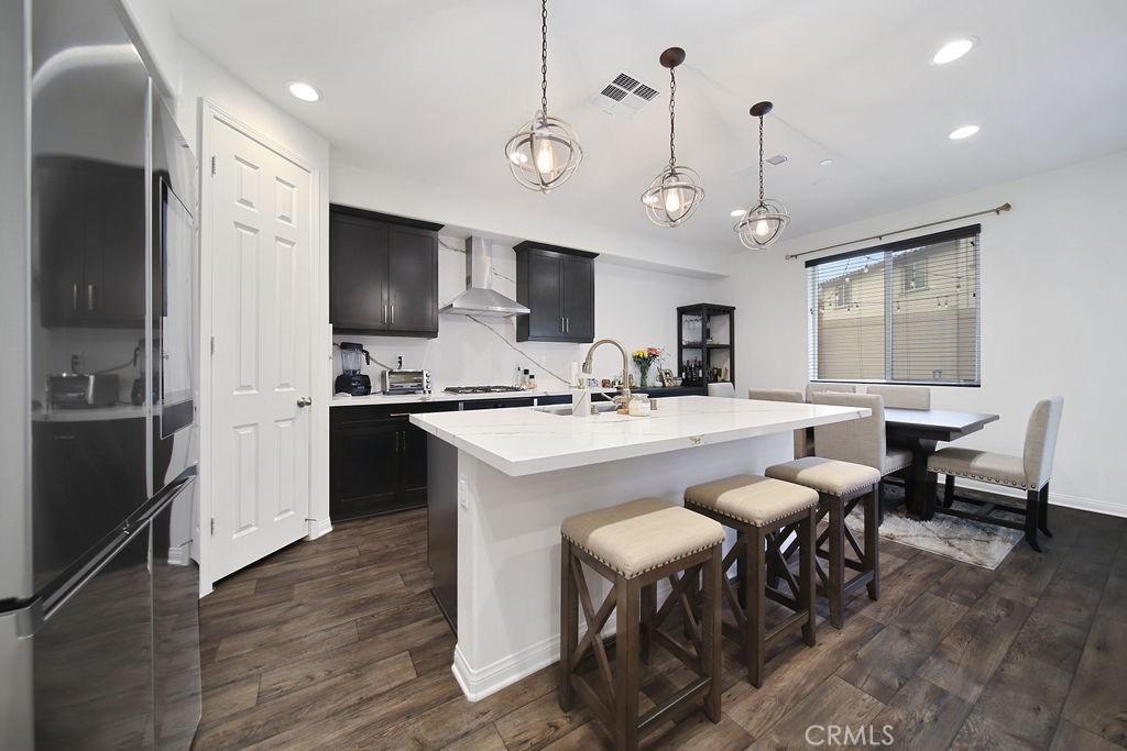 kitchen with a center island with sink, gas cooktop, decorative light fixtures, dark hardwood / wood-style flooring, and wall chimney exhaust hood