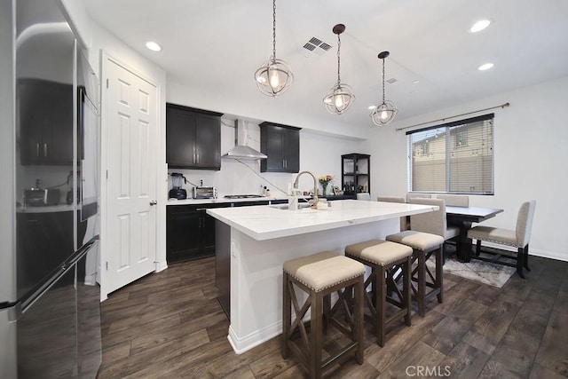 kitchen with a center island with sink, gas cooktop, decorative light fixtures, dark hardwood / wood-style flooring, and wall chimney exhaust hood