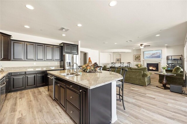 kitchen with sink, light wood-type flooring, a kitchen island with sink, a breakfast bar area, and stainless steel appliances