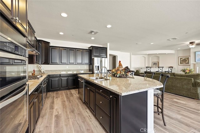 kitchen with a kitchen bar, appliances with stainless steel finishes, a kitchen island with sink, light wood-type flooring, and sink