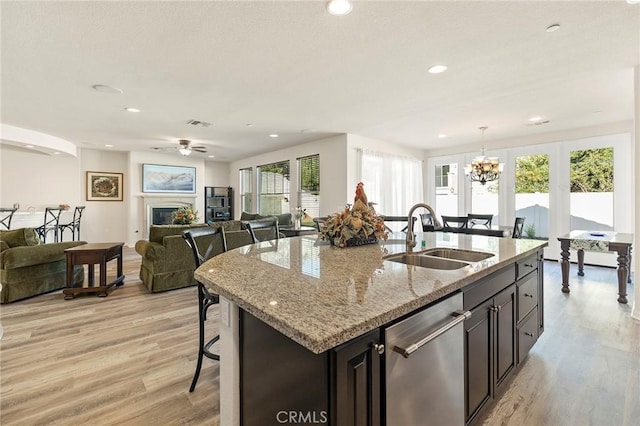 kitchen featuring a kitchen breakfast bar, dishwasher, light stone countertops, pendant lighting, and sink