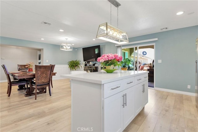 kitchen featuring decorative light fixtures, light hardwood / wood-style flooring, a notable chandelier, a kitchen island, and white cabinetry