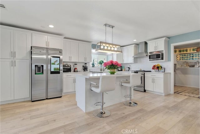 kitchen with white cabinetry, stainless steel appliances, wall chimney range hood, and light hardwood / wood-style floors