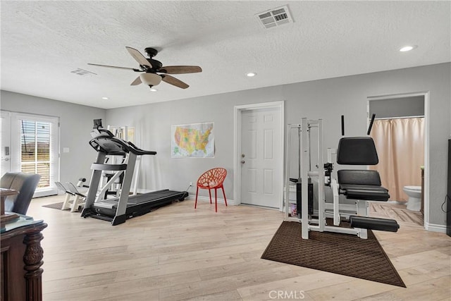 workout area featuring ceiling fan, light hardwood / wood-style flooring, and a textured ceiling