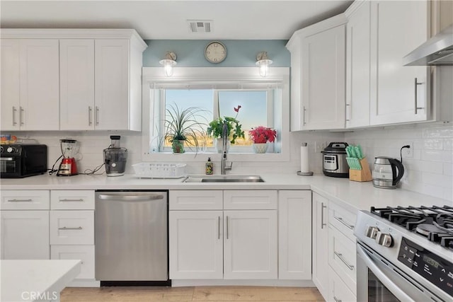 kitchen with wall chimney exhaust hood, sink, white cabinetry, and stainless steel appliances