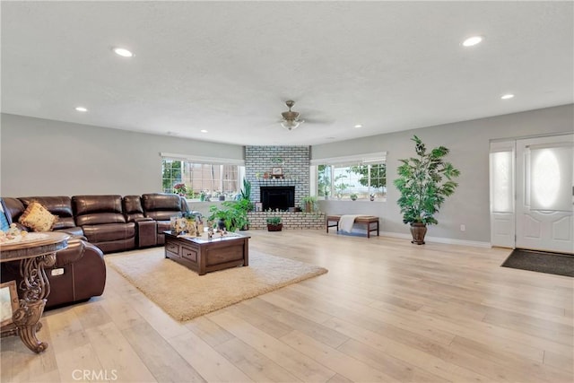 living room with ceiling fan, light wood-type flooring, a wealth of natural light, and a brick fireplace