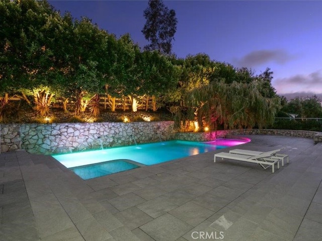 pool at dusk featuring pool water feature and a patio