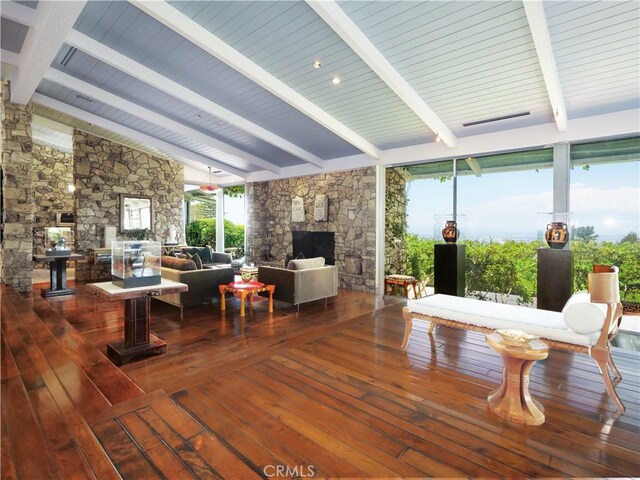 interior space featuring plenty of natural light, wood-type flooring, lofted ceiling with beams, and a stone fireplace