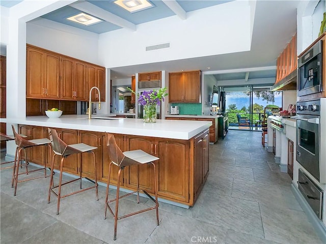 kitchen featuring built in appliances, sink, kitchen peninsula, a breakfast bar, and beam ceiling