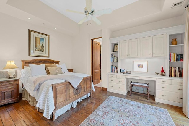 bedroom featuring built in desk, dark wood-type flooring, and ceiling fan