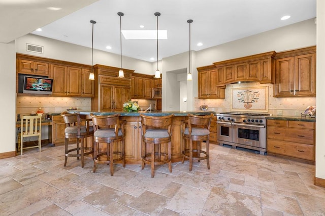 kitchen featuring backsplash, appliances with stainless steel finishes, decorative light fixtures, and a kitchen breakfast bar