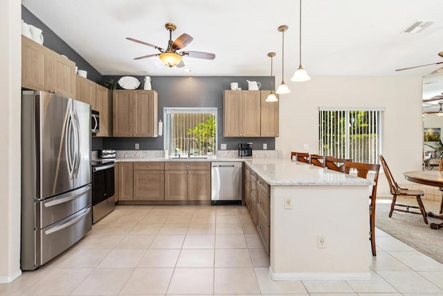 kitchen with kitchen peninsula, a wealth of natural light, light stone counters, and appliances with stainless steel finishes