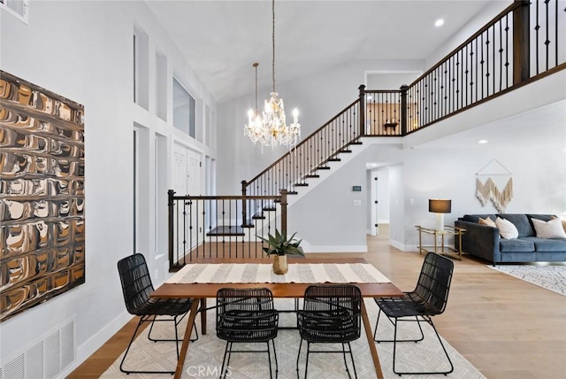 dining space with a notable chandelier, high vaulted ceiling, and light hardwood / wood-style flooring