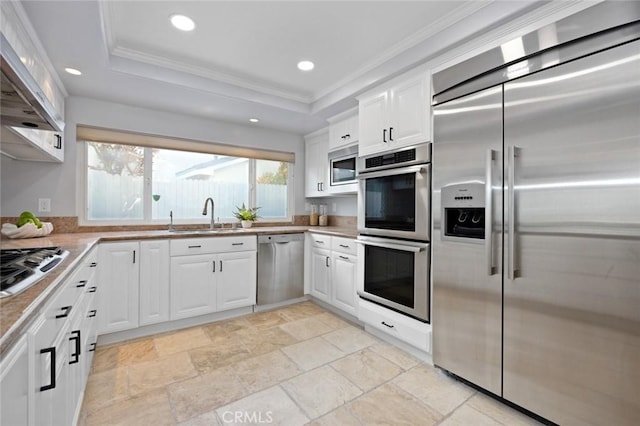 kitchen with ornamental molding, a raised ceiling, sink, built in appliances, and white cabinetry