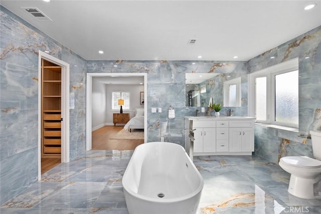 bathroom with vanity, a bath, toilet, and tile walls