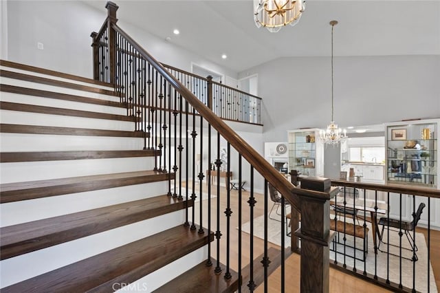 stairway with high vaulted ceiling, a chandelier, and wood-type flooring