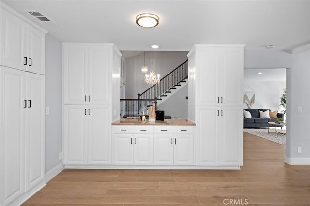 bar featuring pendant lighting, white cabinets, light hardwood / wood-style floors, and a notable chandelier