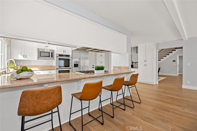 kitchen featuring light wood-type flooring, built in appliances, and white cabinetry