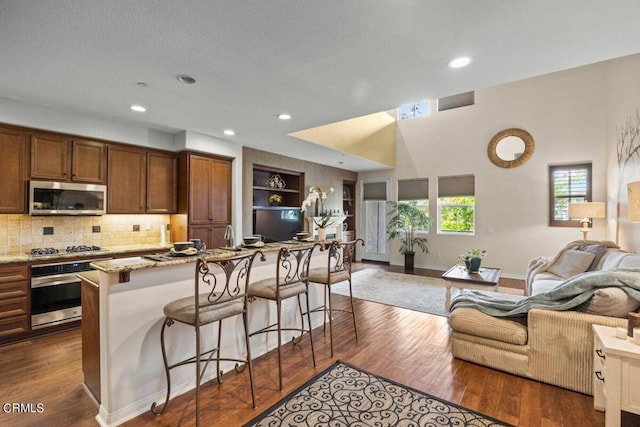 kitchen featuring a kitchen bar, appliances with stainless steel finishes, tasteful backsplash, light stone counters, and dark hardwood / wood-style floors