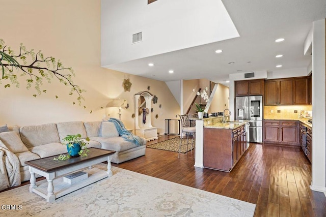 kitchen featuring a center island with sink, stainless steel refrigerator with ice dispenser, a breakfast bar area, and dark hardwood / wood-style flooring