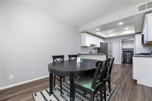 dining space with independent washer and dryer, dark hardwood / wood-style flooring, and a tray ceiling