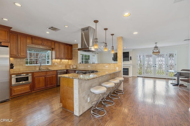 kitchen with decorative light fixtures, kitchen peninsula, exhaust hood, tasteful backsplash, and hardwood / wood-style floors