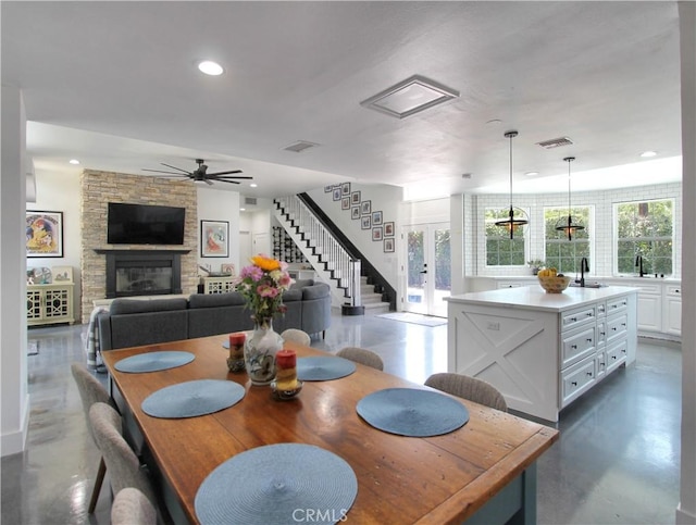 dining space featuring french doors, a stone fireplace, ceiling fan, and sink