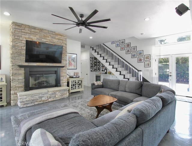 living room featuring concrete flooring, french doors, a stone fireplace, and ceiling fan