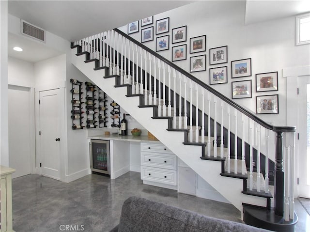 staircase with bar, concrete floors, and beverage cooler