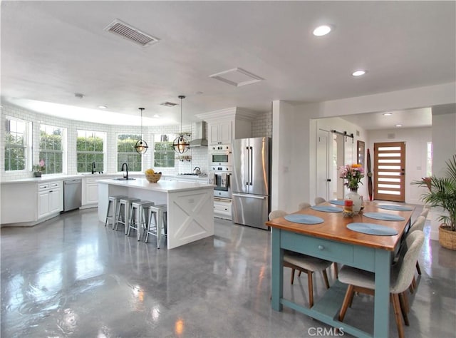 kitchen with stainless steel appliances, a barn door, white cabinets, a center island, and hanging light fixtures