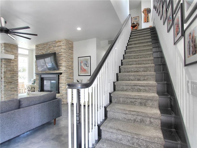 stairway featuring ceiling fan, a fireplace, and concrete floors